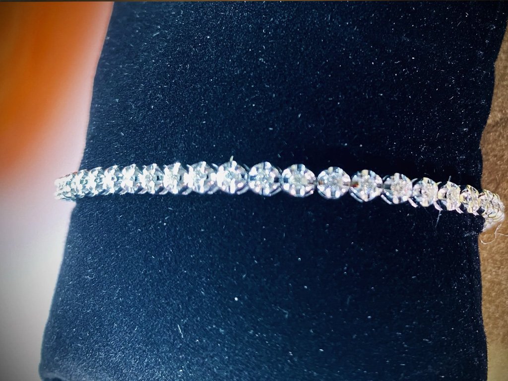 Close-up photo of a diamond tennis bracelet with clear round-cut stones, displayed on black fabric.