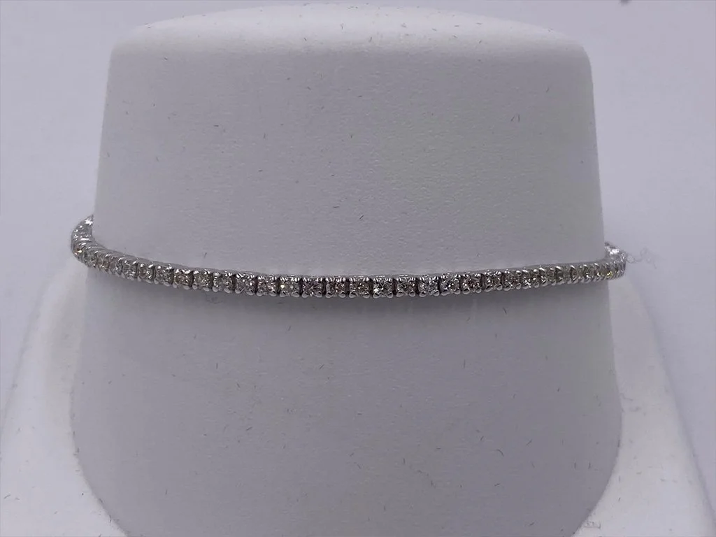 Silver bracelet with small clear stones displayed on a white stand.