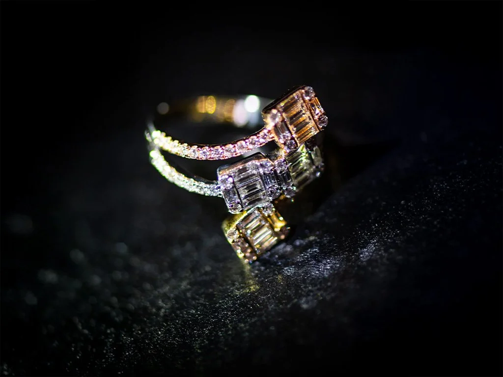 A ring with clear rectangular and square gemstones, possibly diamonds, on a black reflective surface.