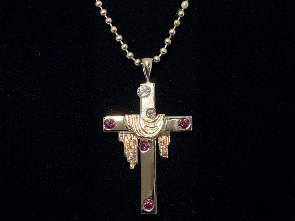 A silver necklace with a cross pendant adorned with pink and clear gemstones, displayed against a black background.