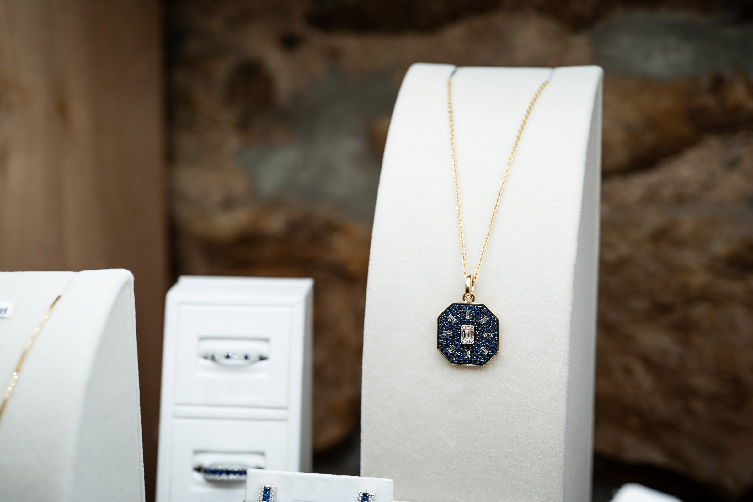 A gold necklace with a navy and diamond pendant displayed on a white jewelry stand.