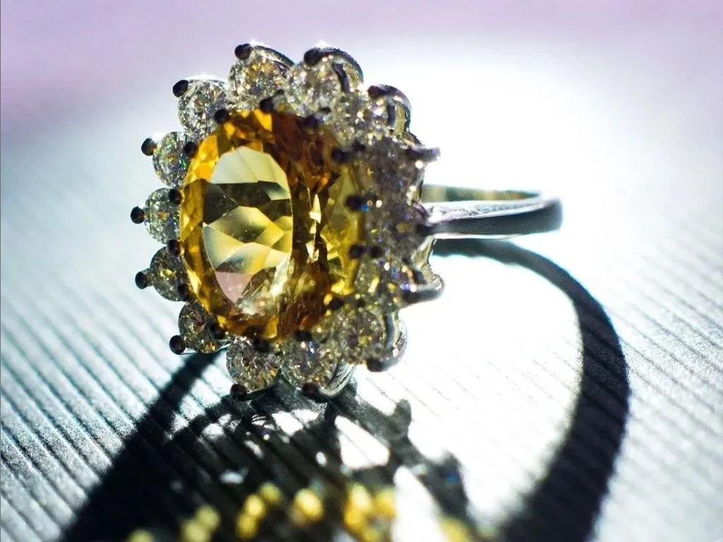 Ring with a yellow gemstone surrounded by smaller clear gemstones on a textured surface.