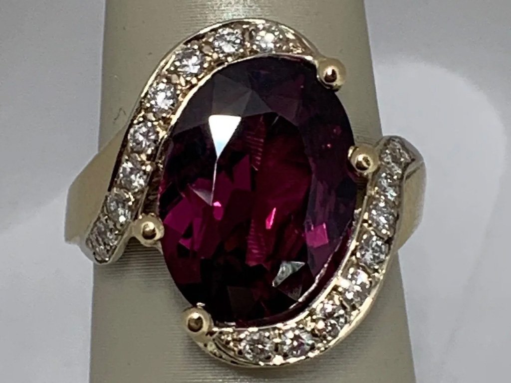 A gold ring with a large oval-shaped deep red gemstone, surrounded by a halo of small diamonds.