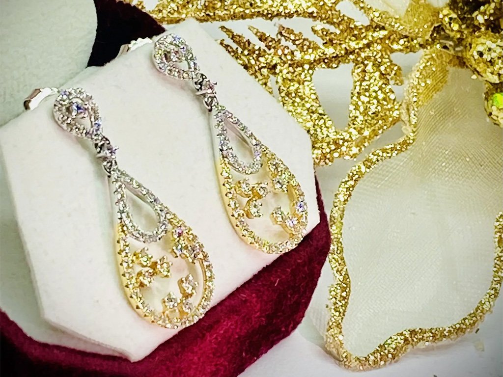 Gold and silver rhinestone jewelry set with earrings and a necklace displayed on a white fabric cushion and decorative gold-colored ribbon.