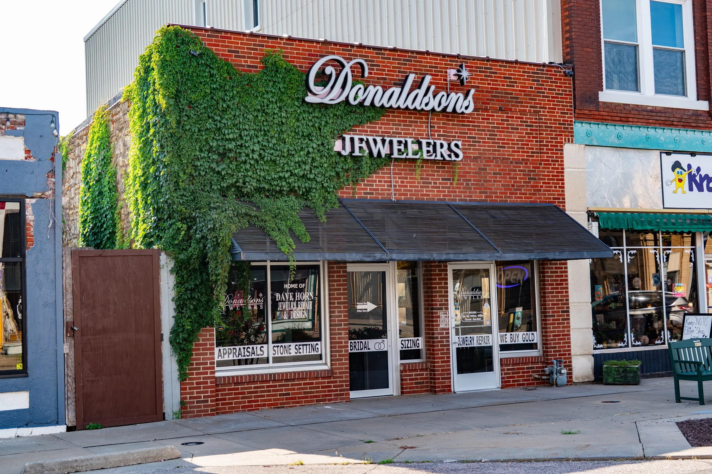 Exterior view of Donaldson's Jewelers storefront with brick facade, greenery growing on the wall, and signs indicating jewelry services like appraisals, stone setting, bridal, sizing, and gold buying.
