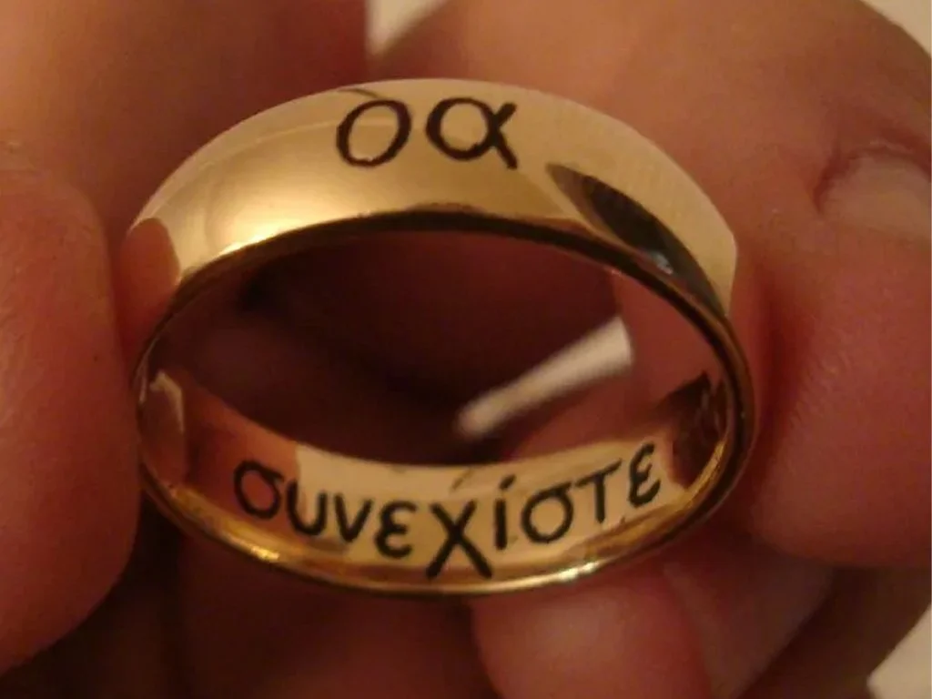 Close-up of a shiny gold ring with an engraved message and a reflective surface showing the reflection of the wearer.