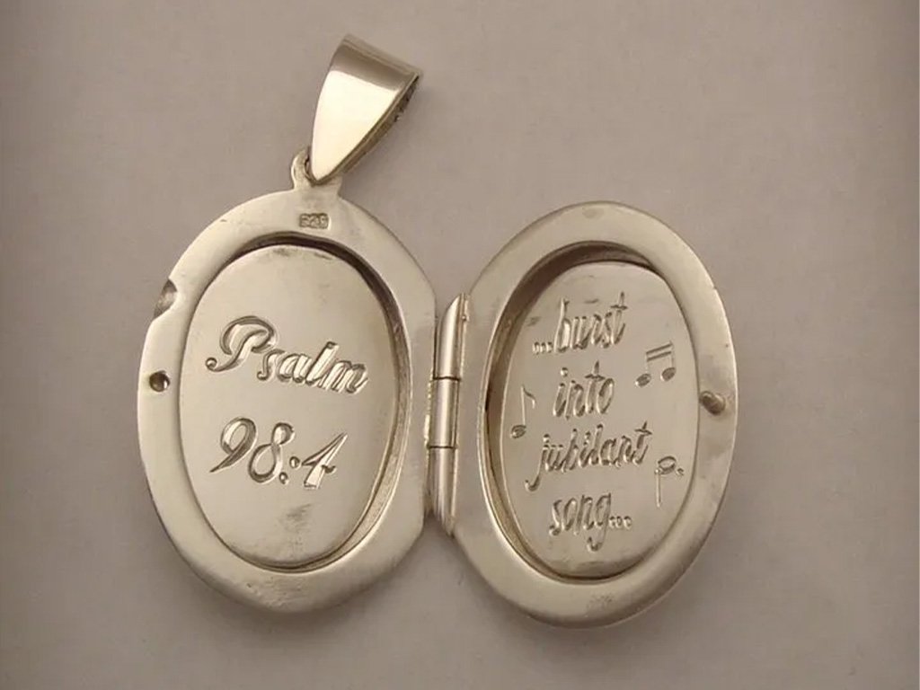 A silver locket shaped like a compact mirror with engraved words: "Palma 98.4" on the left side and "Just into juicet at song" on the right side. The locket is open, showing the engraved inside surfaces.