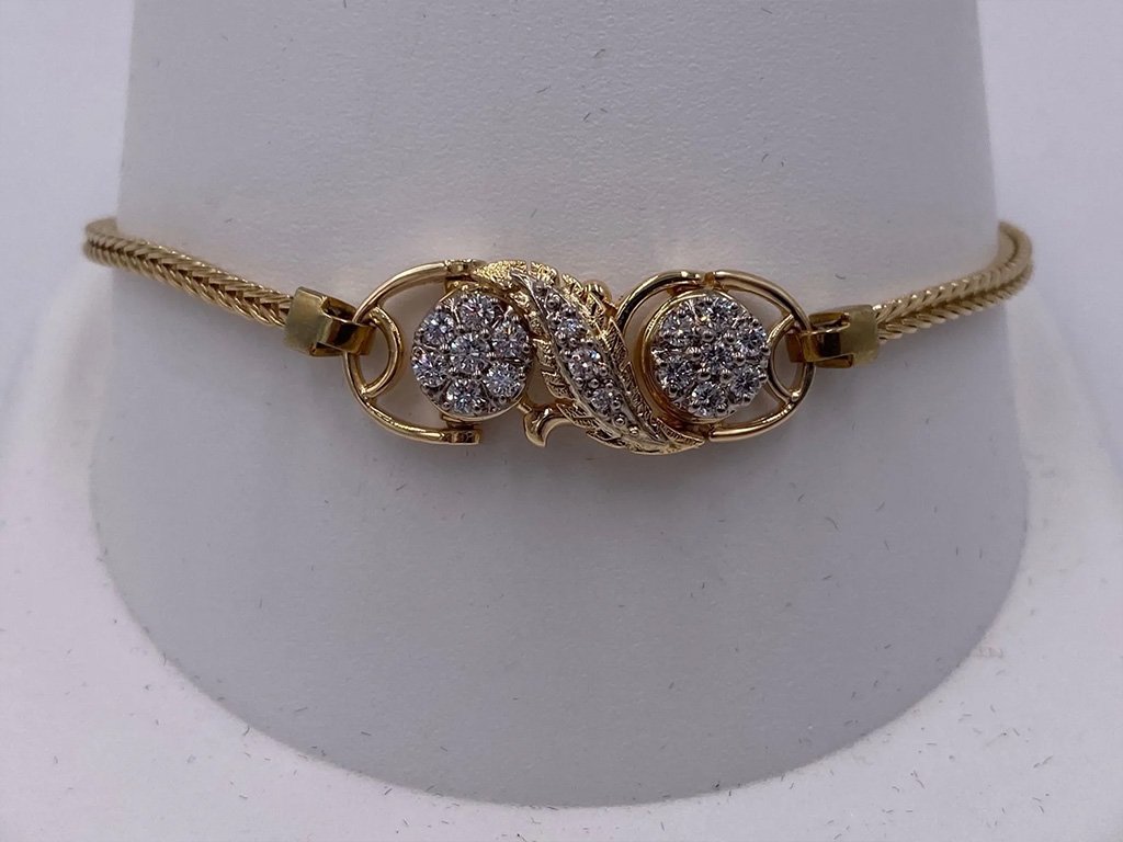 Gold bracelet with decorative clasp featuring two circular elements of small diamonds and a curved gold detail.