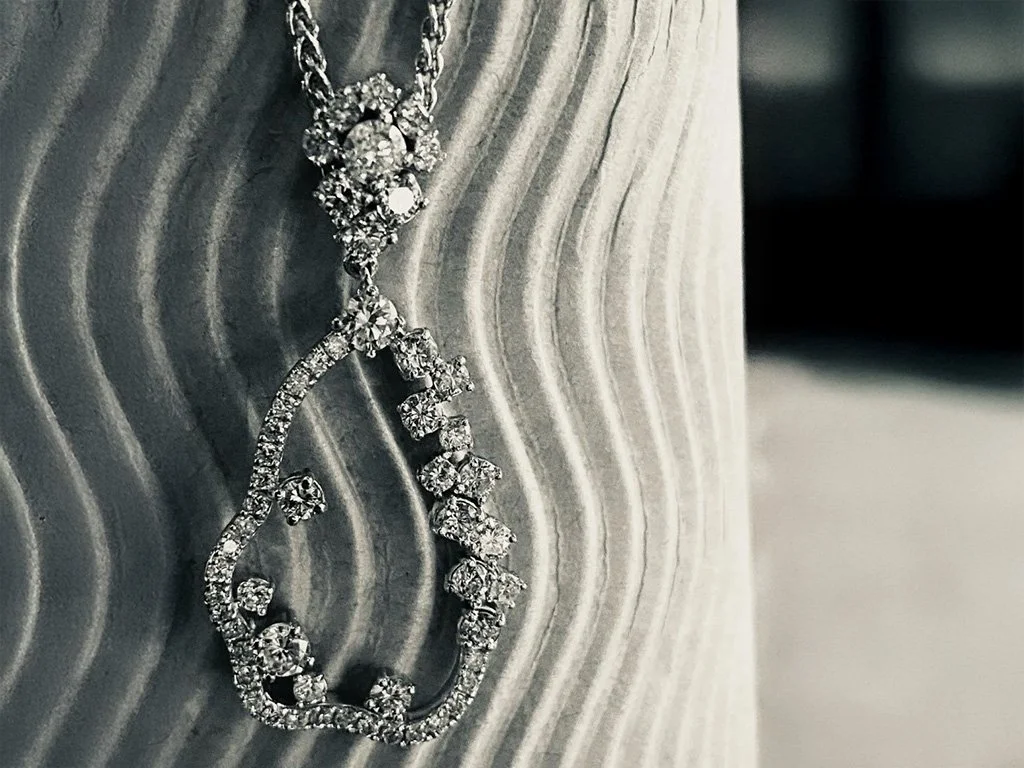 Close-up of a silver diamond necklace with a pendant in the shape of a musical note on a textured gray surface.