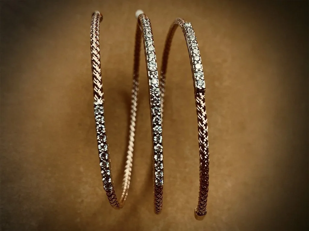 Three gold bangles with embedded diamonds on a brown background.