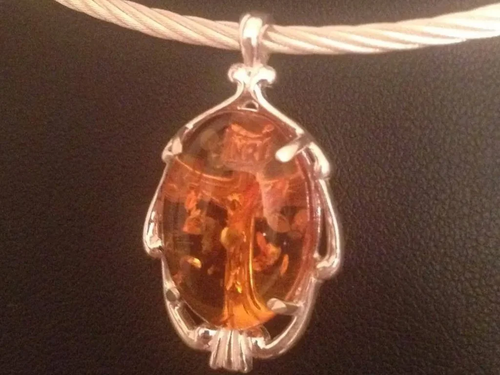 A pendant necklace with an amber pendant framed in a silver setting, hanging from a white cord.