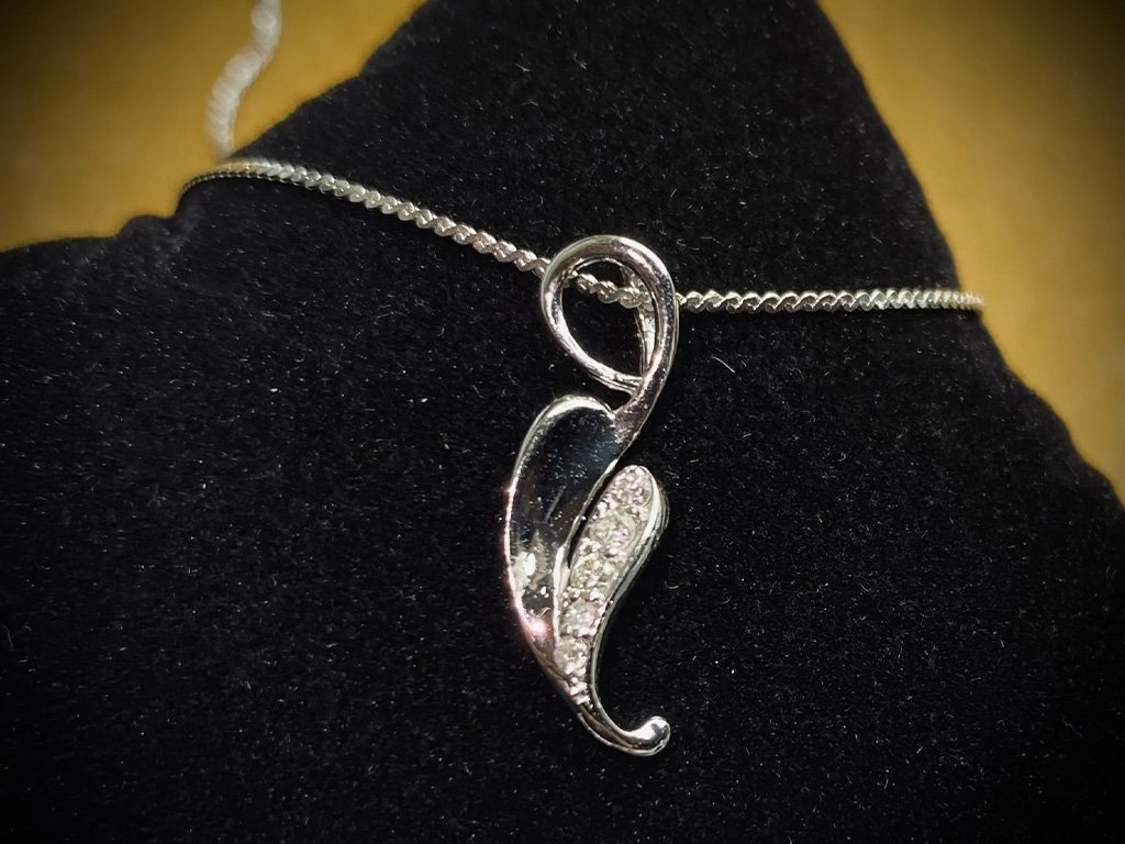 A silver necklace with a pendant shaped like a treble clef decorated with small gemstones, displayed on a black surface.