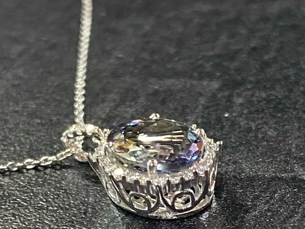 A silver necklace with a pendant featuring an oval-shaped gemstone surrounded by intricate filigree detailing.