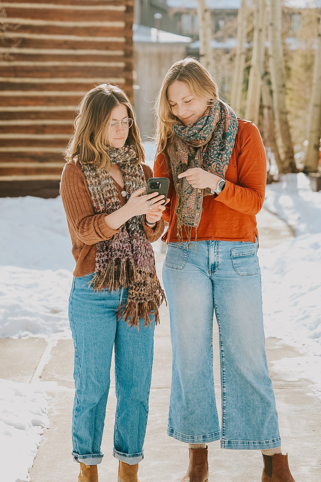 leah and kia of aspen alley creative stand looking at a phone in the snow