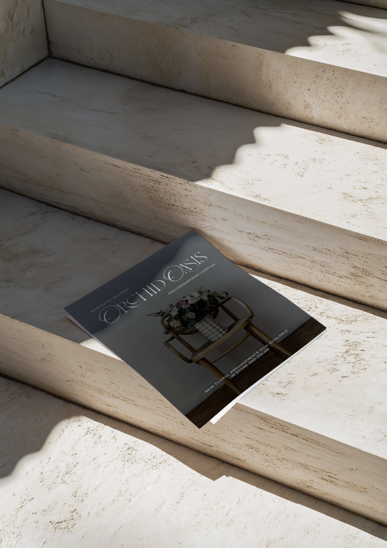 A magazine titled 'Orchid & Oasis' resting on a white stone staircase with sunlight casting shadows.