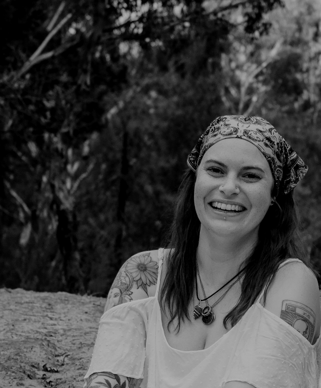 Smiling woman with tattoos and a patterned headscarf outdoors in black and white.