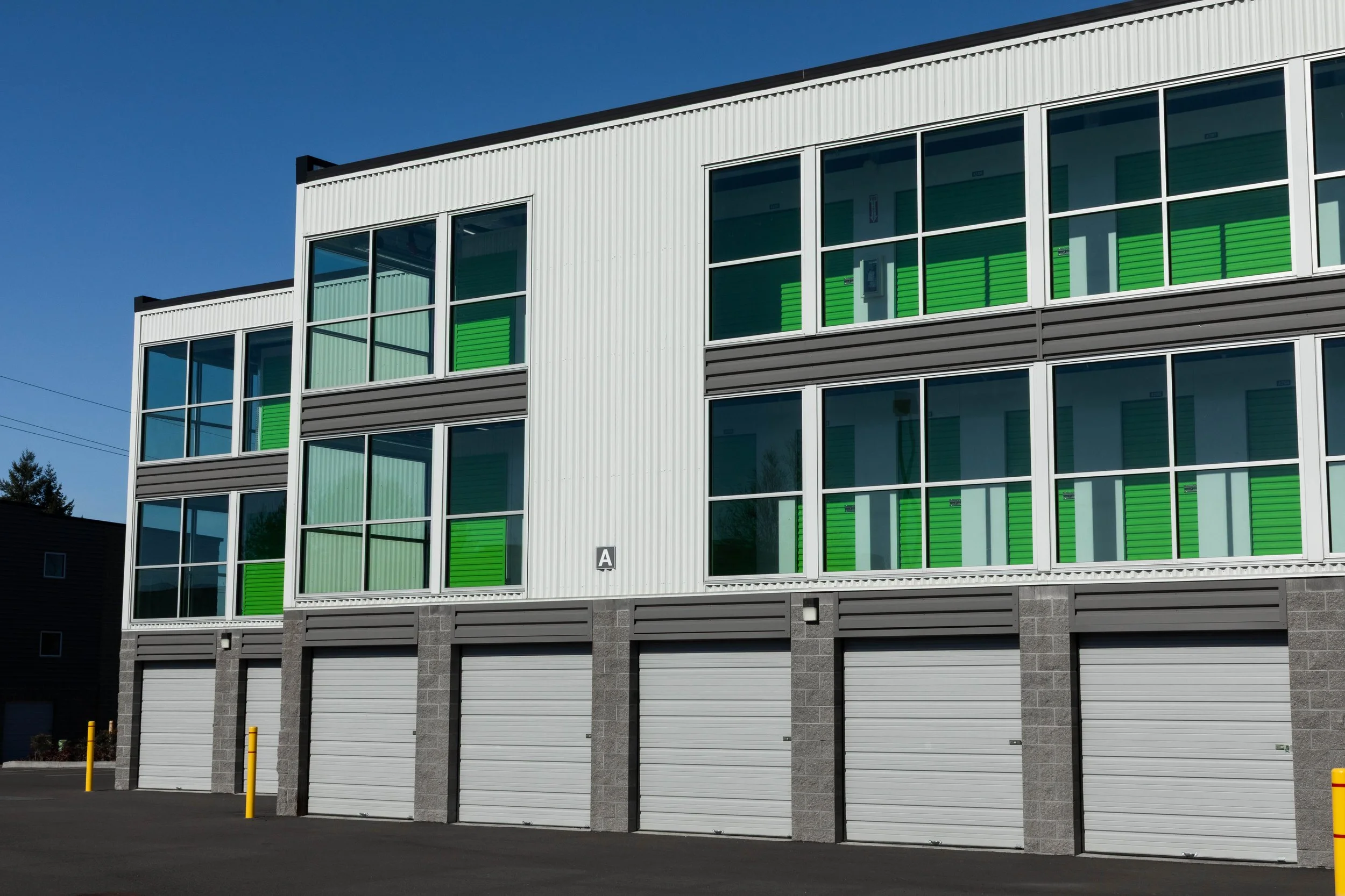 Modern building with multiple levels, green window shutters, large glass windows, and garage doors at the bottom.