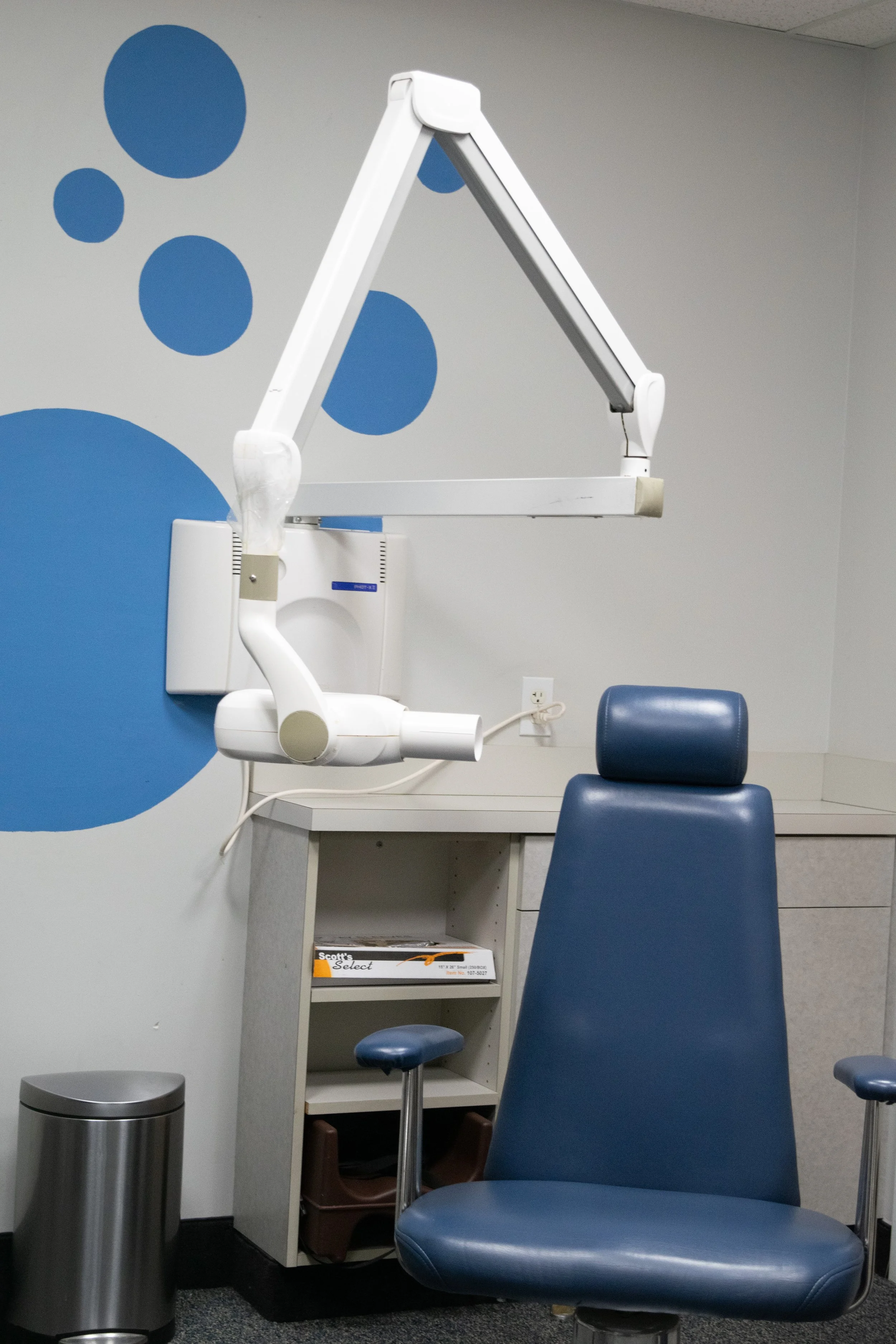Dental chair in a medical examination room with a mounted x-ray machine overhead.