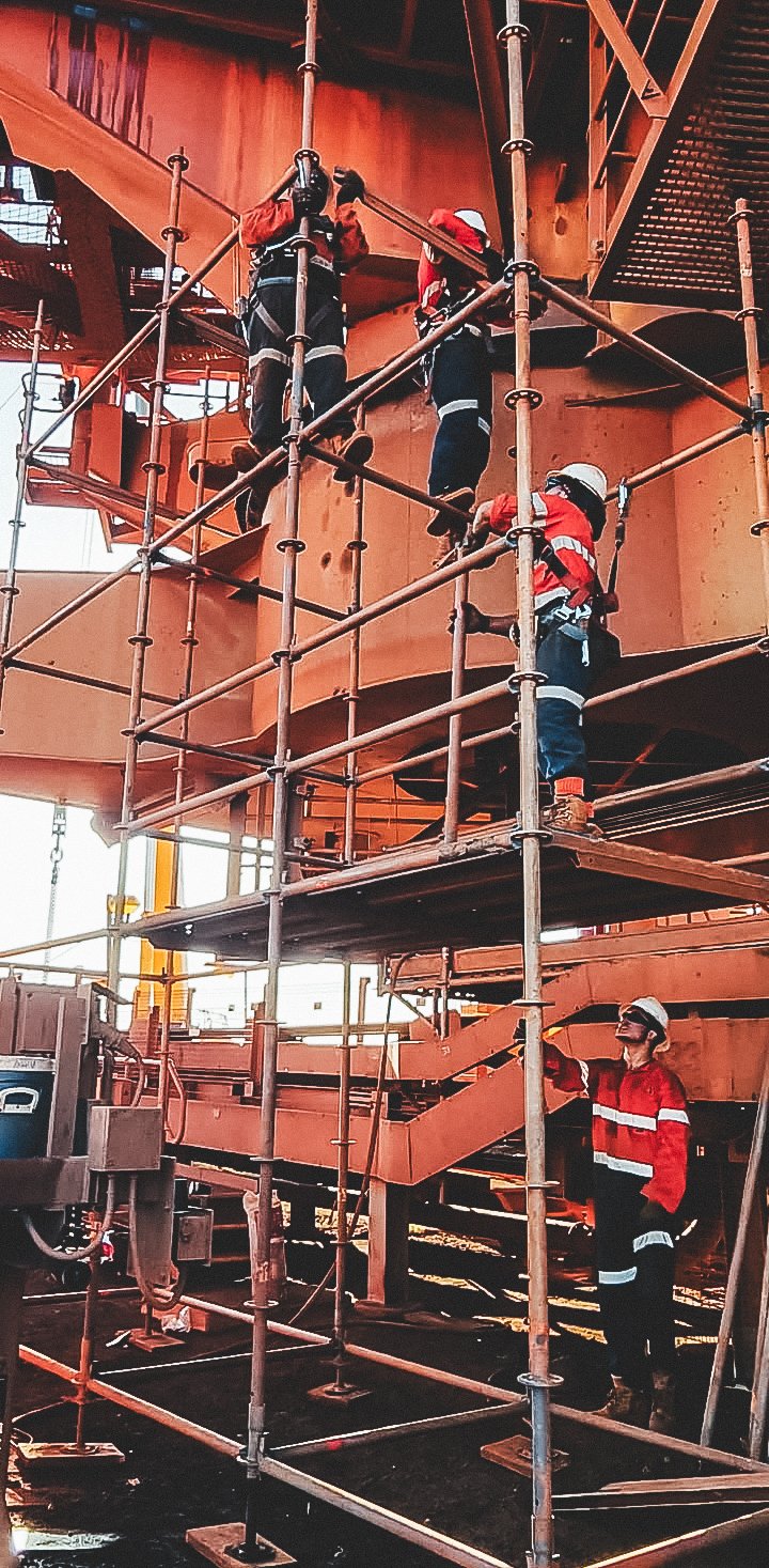 Construction workers wearing safety gear working on scaffolding around a large industrial structure.