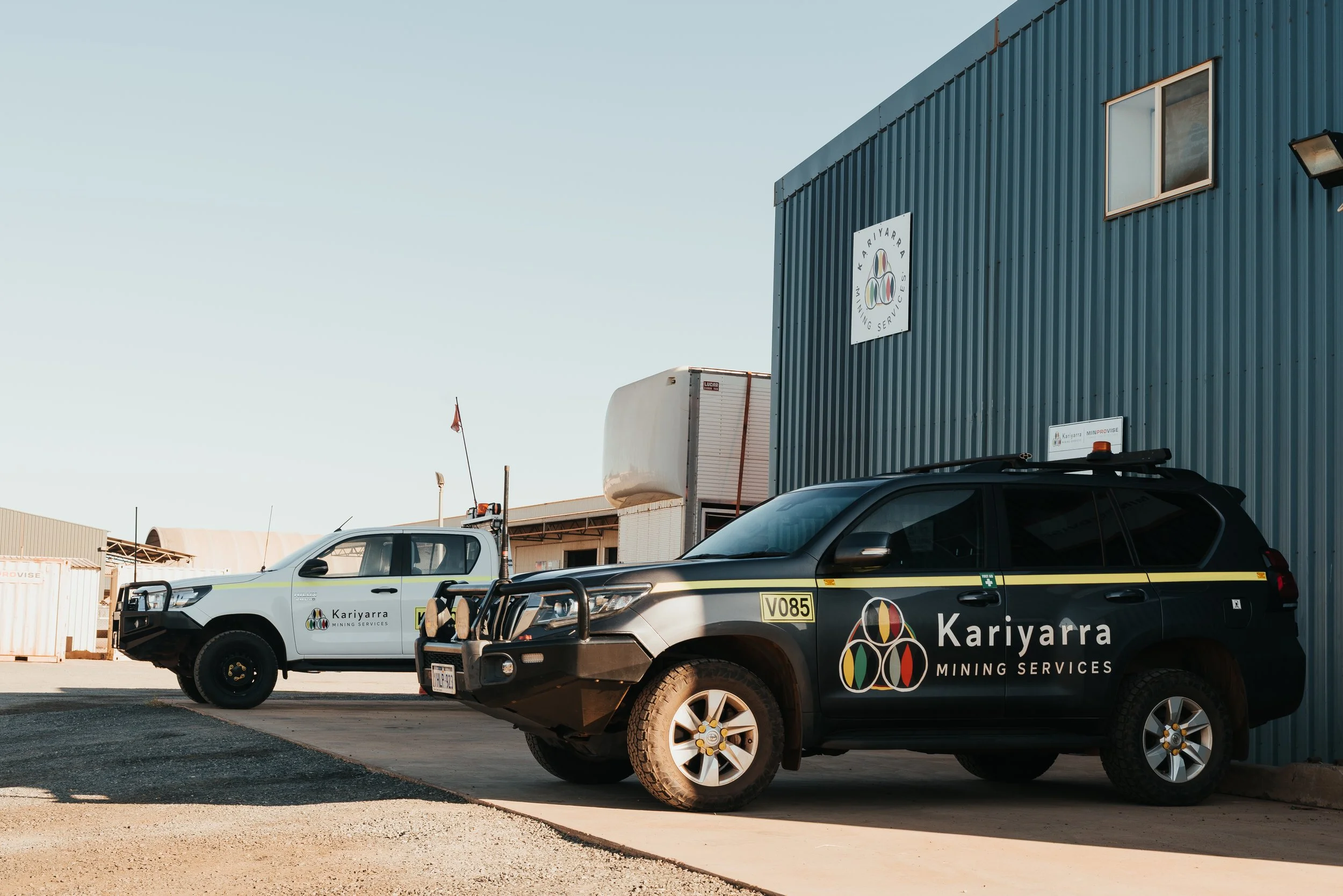 Two Kariyara Mining Services vehicles parked outside a blue industrial building during daytime.