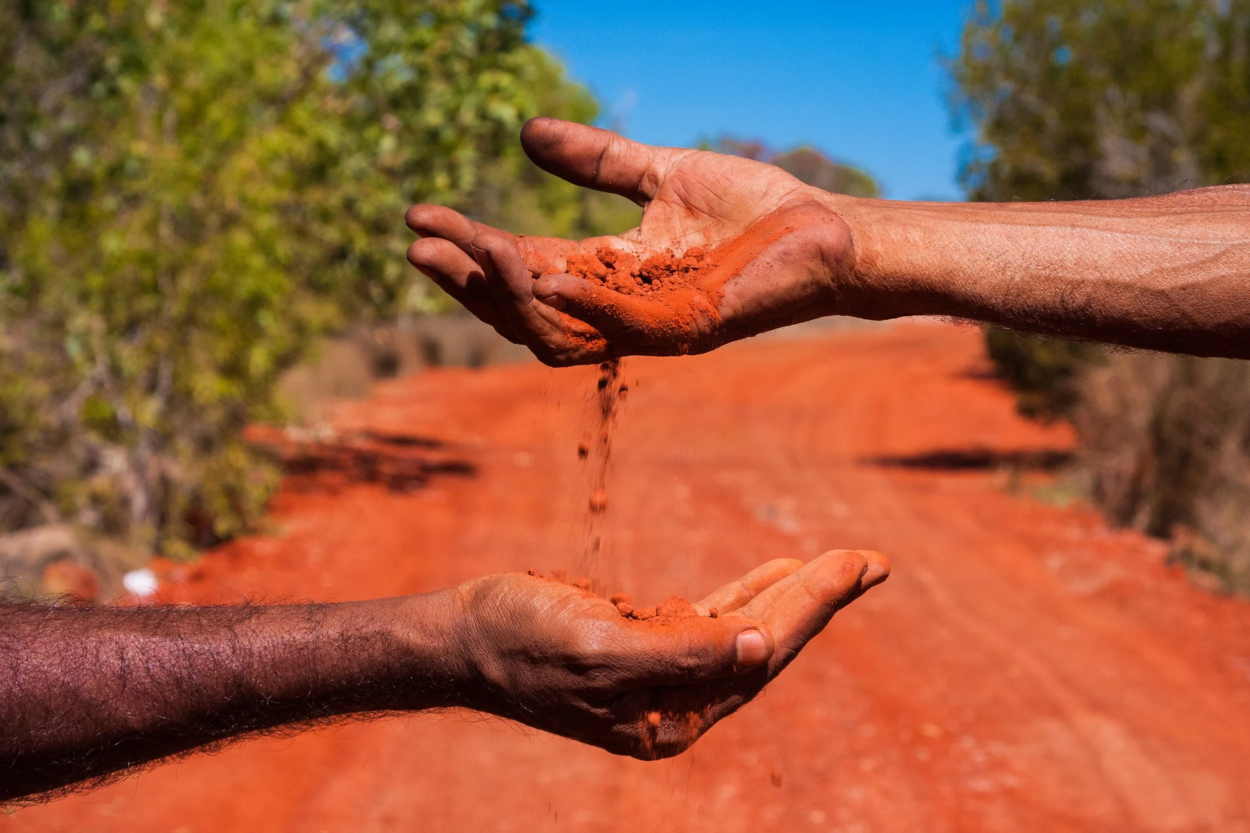 Two hands passing red clay or dirt between each other outdoors on a sunny day