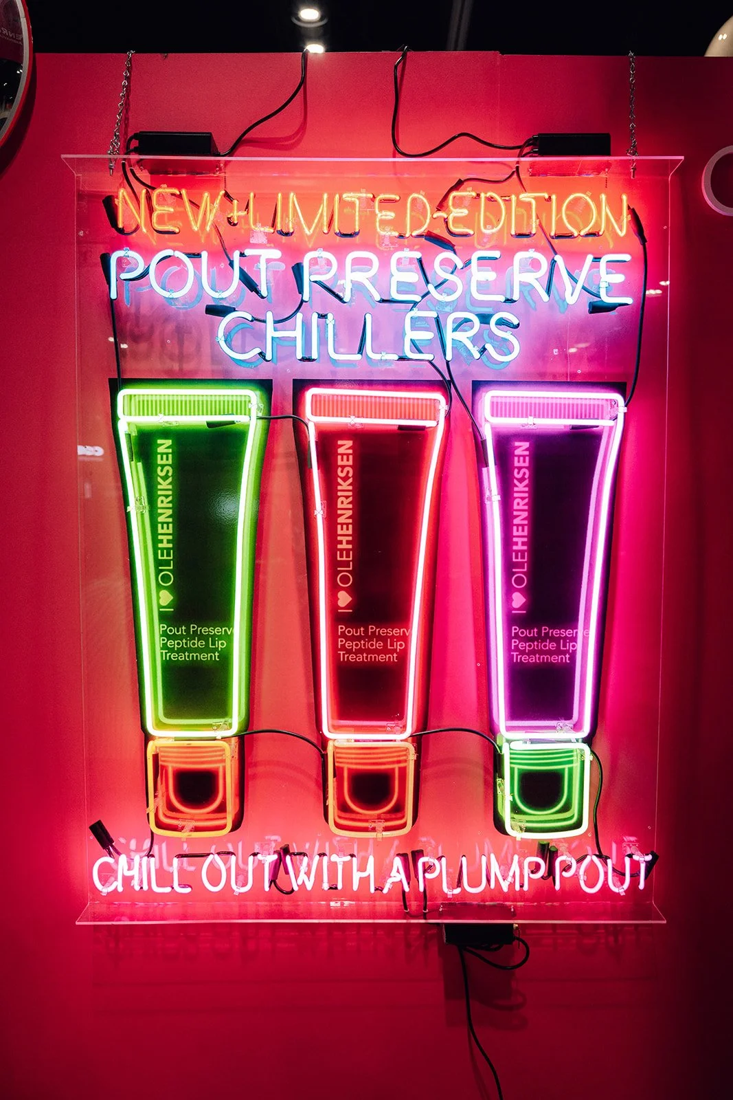 Neon sign with the text 'New Limited Edition Pouf Reserve Chillers' and three colorful illuminated tubes labeled 'Oleh Henriksen Pout Preserv Peptide Lip Treatment' with the phrase 'Chill Out With a Plump Pout' at the bottom.
