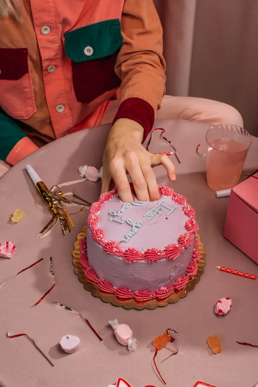 Woman's hand pressing into the frosting of a lavender birthday cake, an image of the sudden emotional flood of rejection sensitive dysphoria