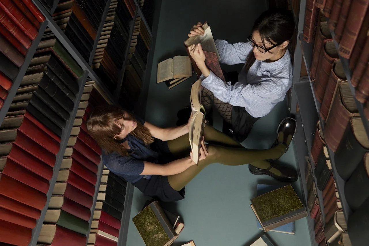 Two women body doubling in a library, working quietly side by side between the stacks — a focus strategy for adults with ADHD.