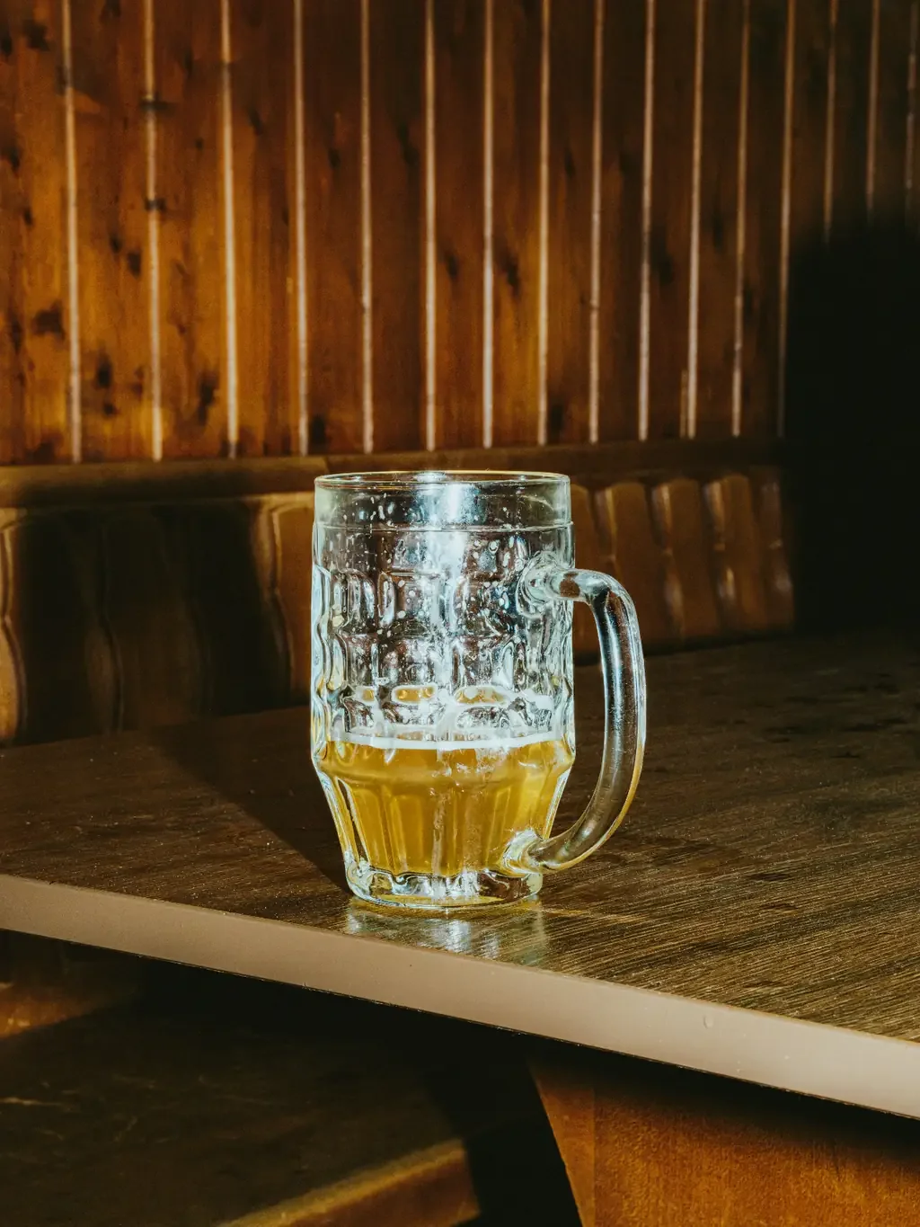 Half-finished glass mug of beer on a wooden table in an empty bar booth with wood-paneled walls.