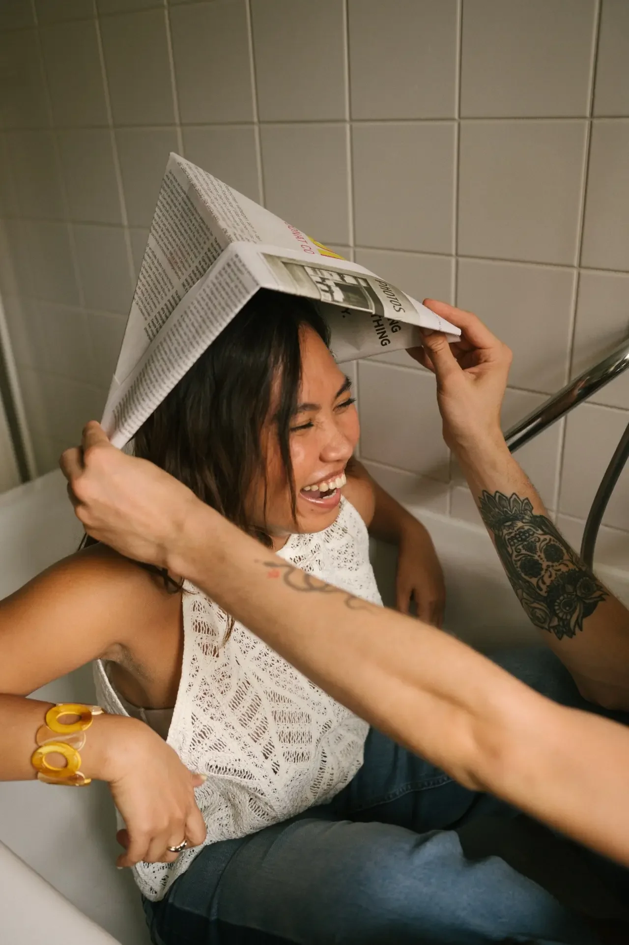 Woman laughing as a friend holds a newspaper tent over her head, showing ADHD friendships built on shared silliness.