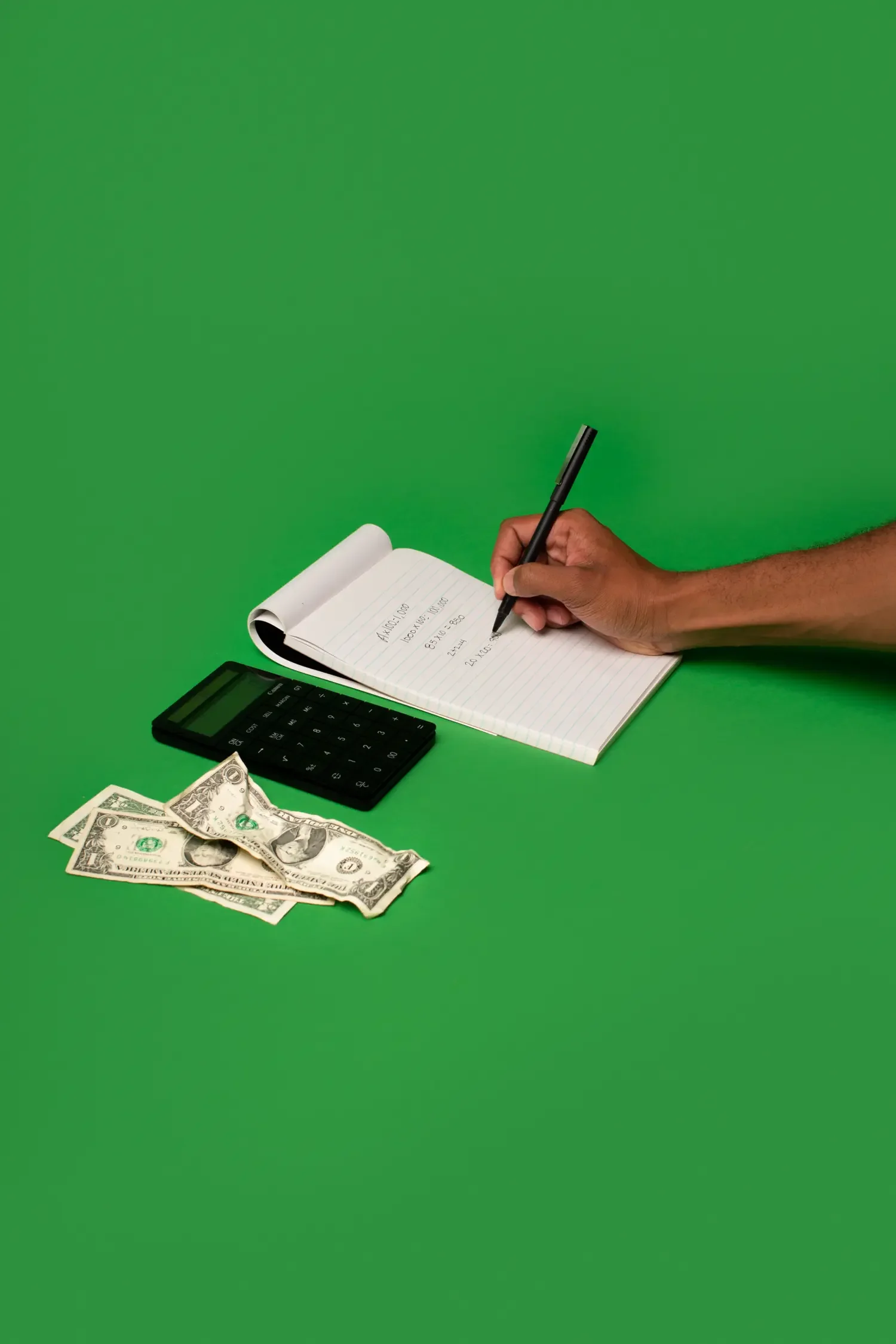 Hand writing cost calculations on a notepad next to a calculator and dollar bills, tallying the ADHD tax.