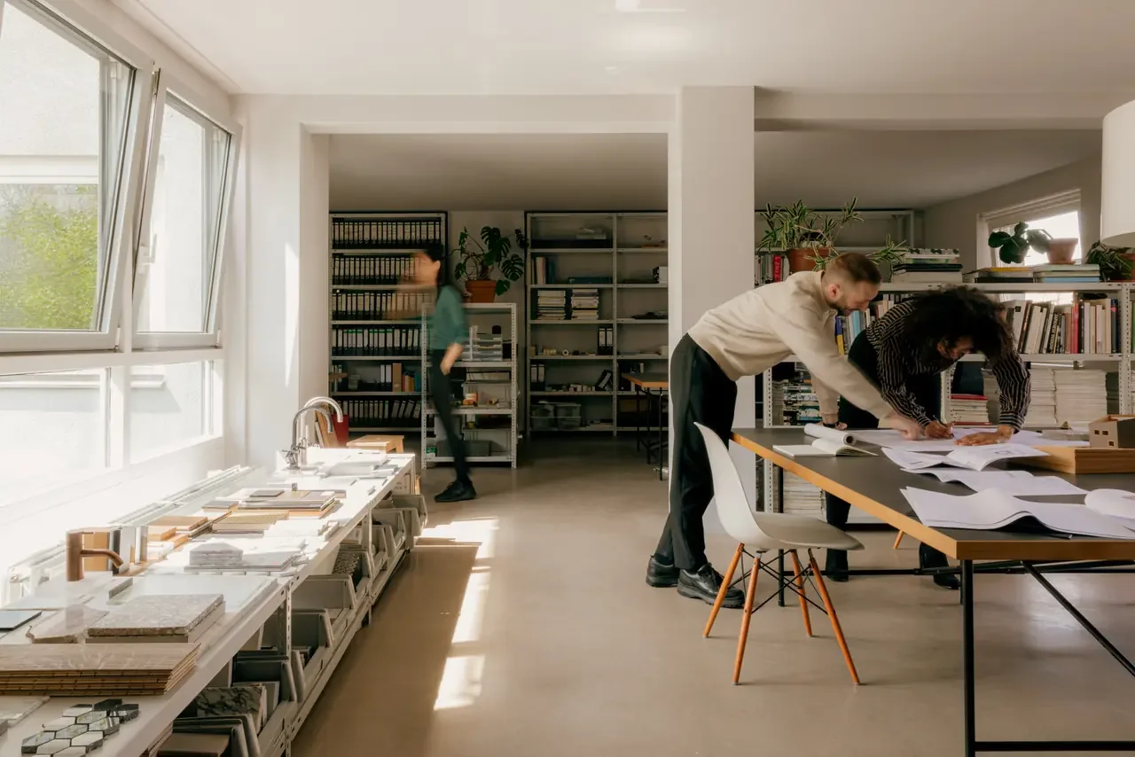 Sunlit design studio with three colleagues at work — the visible room where high-functioning ADHD output gets graded