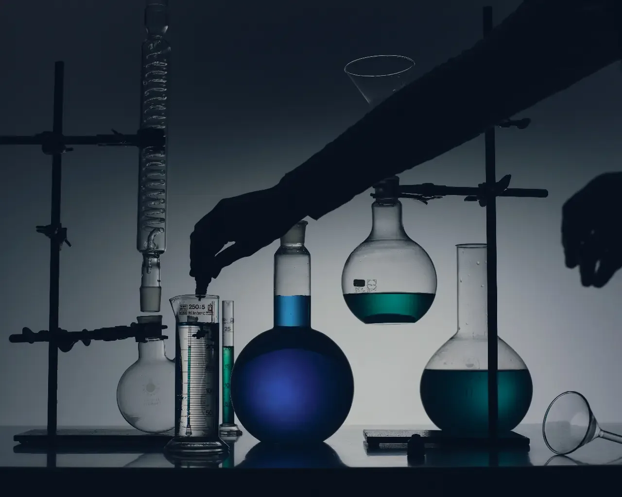 Silhouetted hands adjusting glass flasks of blue liquid in a dim lab, suggesting the depleted stage of ADHD burnout at work.