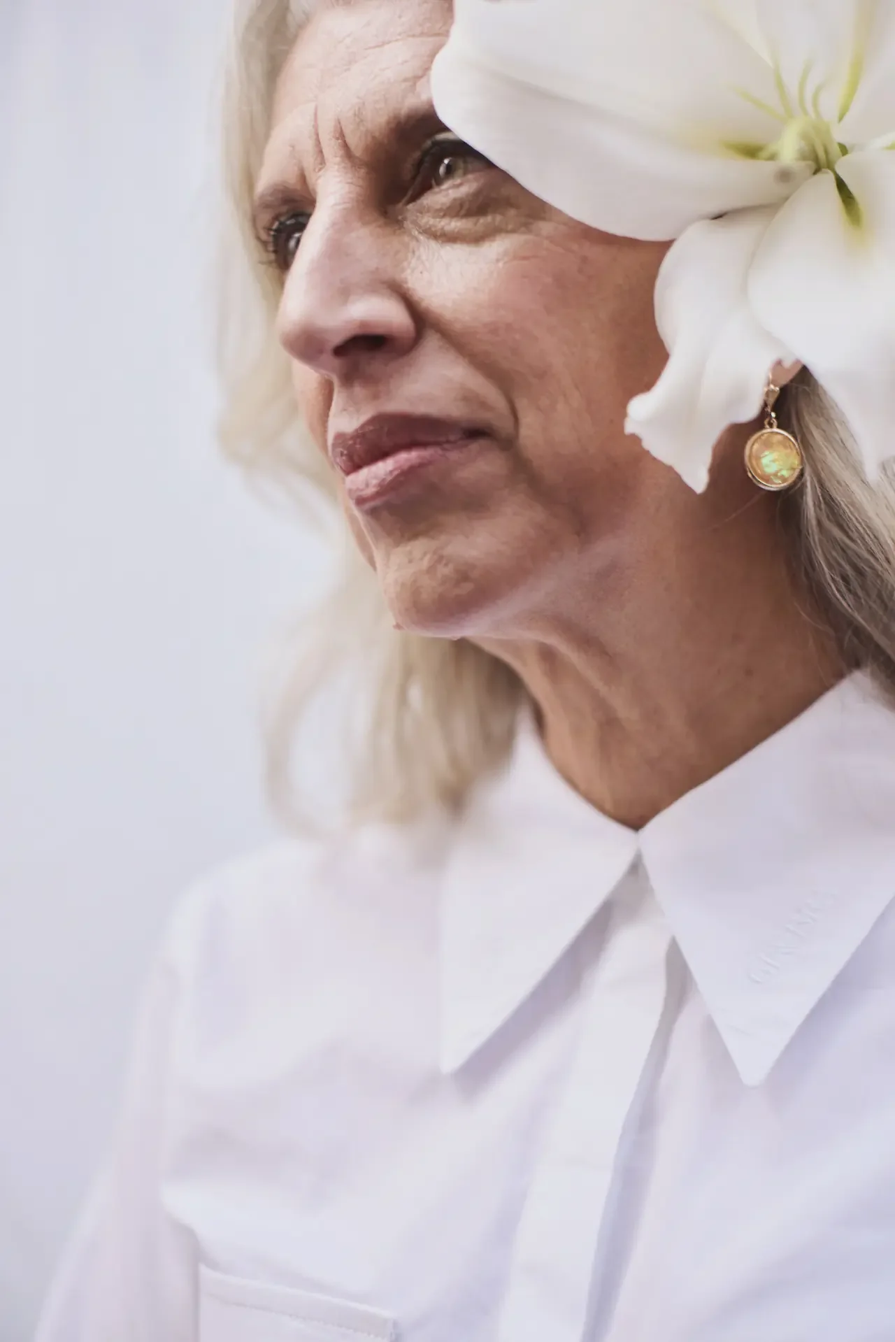Older woman with silver hair and a white lily tucked behind her ear, gazing thoughtfully into the distance, reflecting on a late ADHD diagnosis.