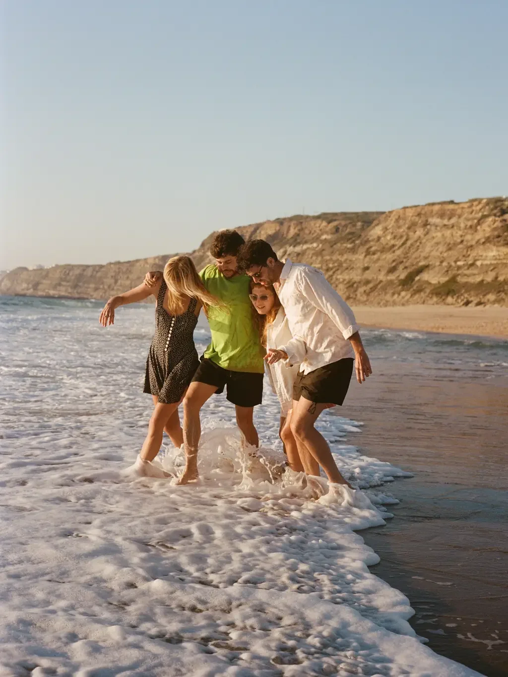 Four friends walking arm in arm through the surf on a sunny beach — ADHD friendships thrive on presence, even when texts go unanswered