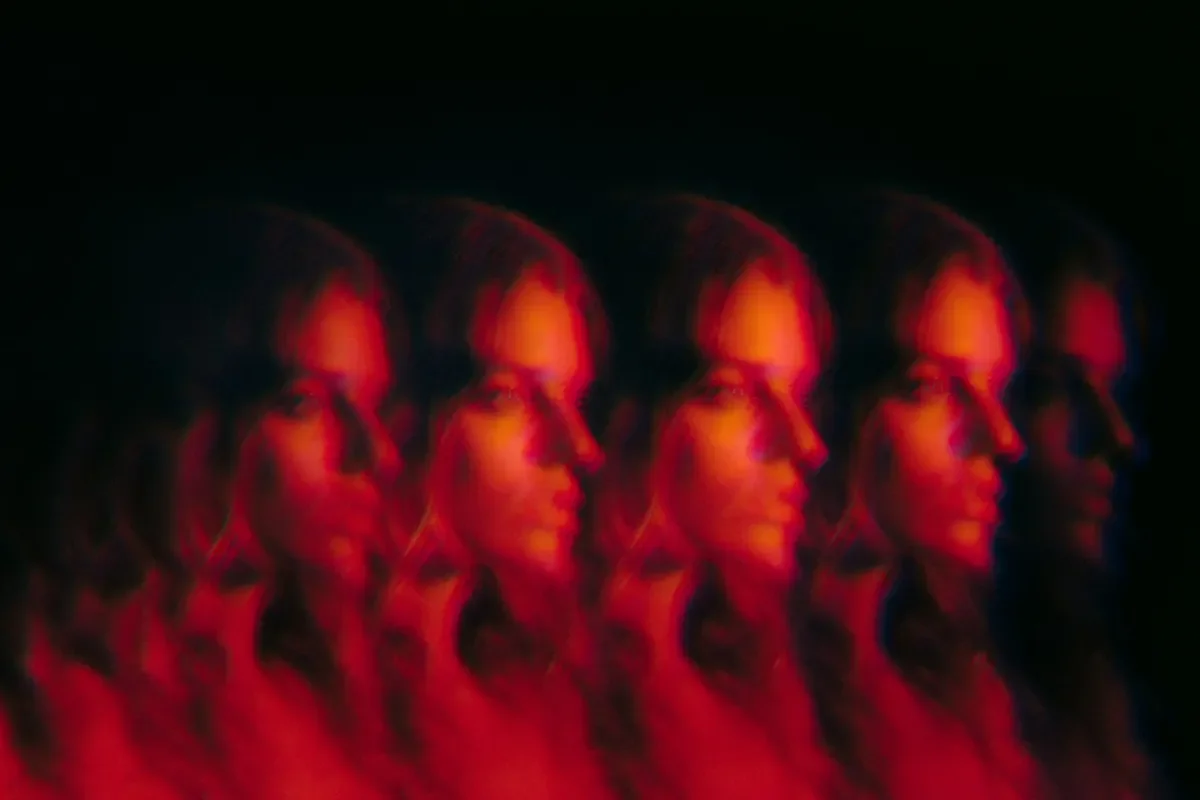 The same woman's profile repeated five times in a blurred row, lit in red against a black background.