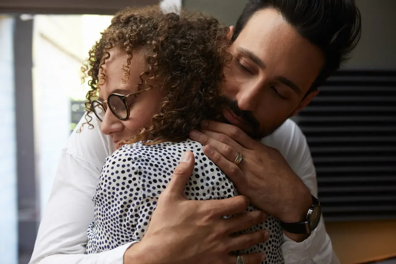 A couple embraces tightly after a conflict, the man's eyes closed as he holds his partner close.