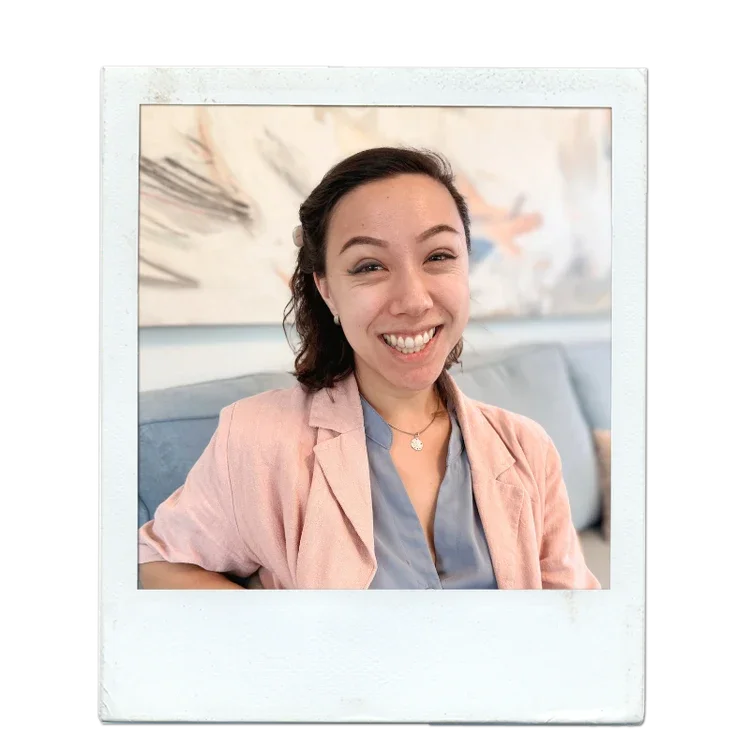 A woman smiling and sitting on a couch with art hanging on the wall behind her.