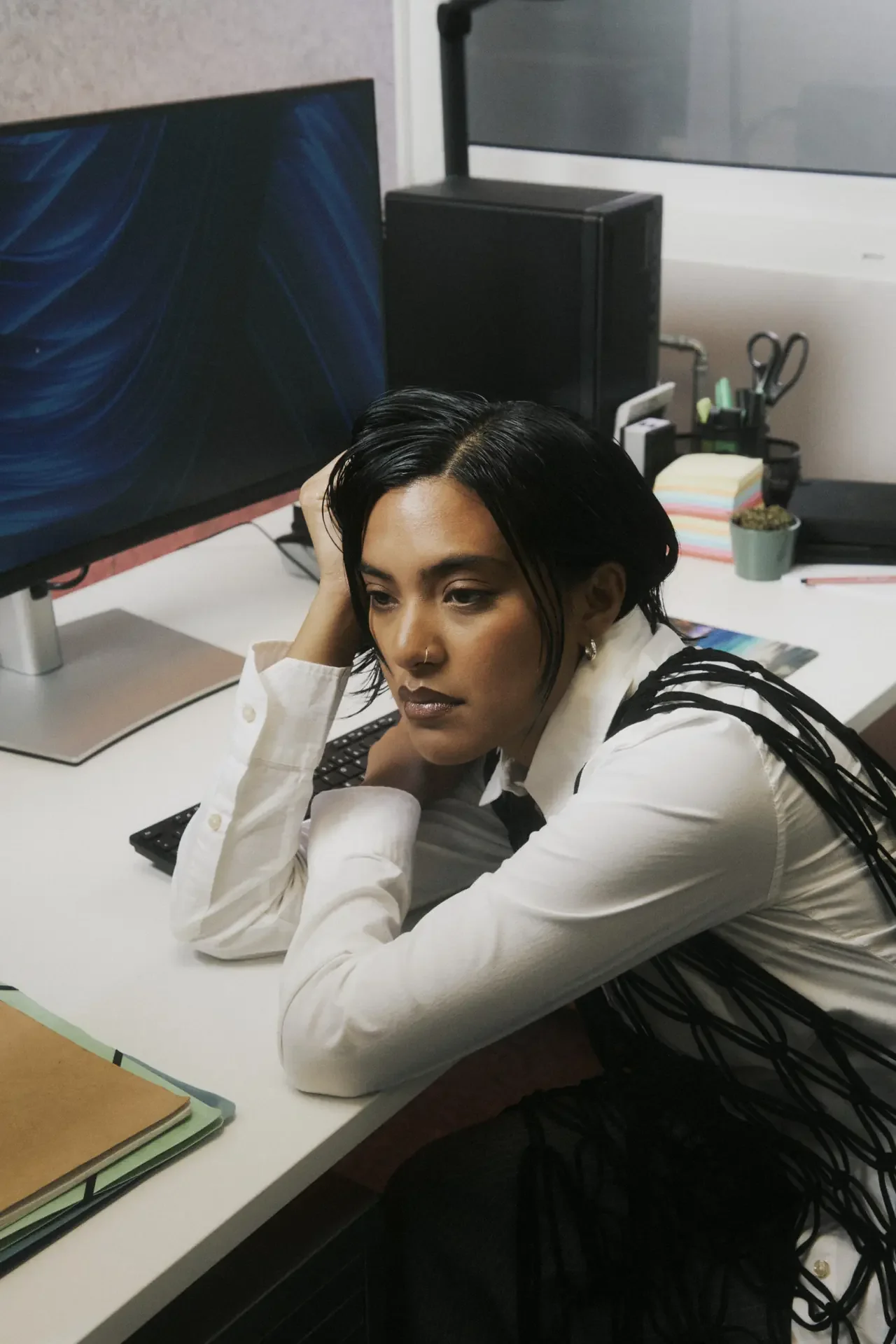 Woman resting her head on her hand at an office desk, staring blankly past her computer monitor, showing the exhaustion of ADHD burnout at work