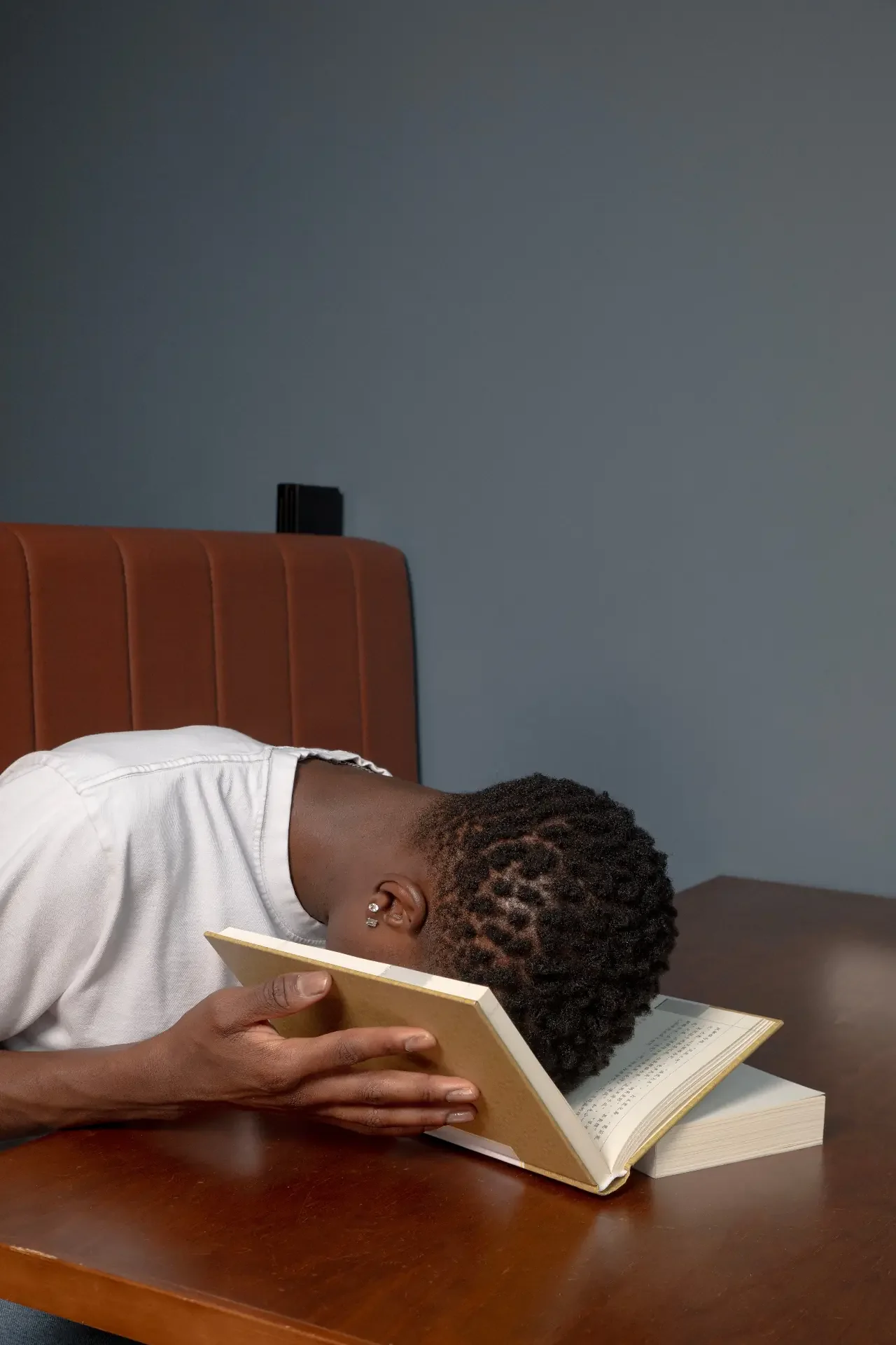 Person in a white shirt with their head face-down in an open book on a wooden table, showing the afternoon energy crash that often comes with ADHD.