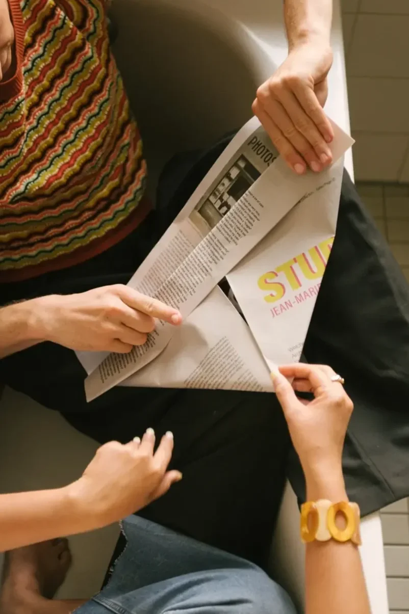 Two friends folding newspaper hats together, an example of making friends with ADHD through structured shared activity