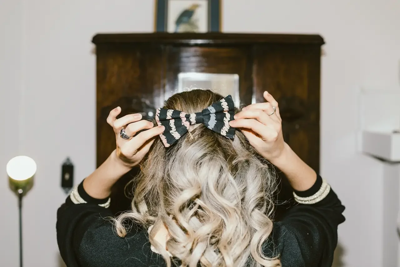 Woman from behind adjusting a hair bow on the top of her head with both hands, illustrating the small-detail precision that quietly drives perfectionism in adults with ADHD.