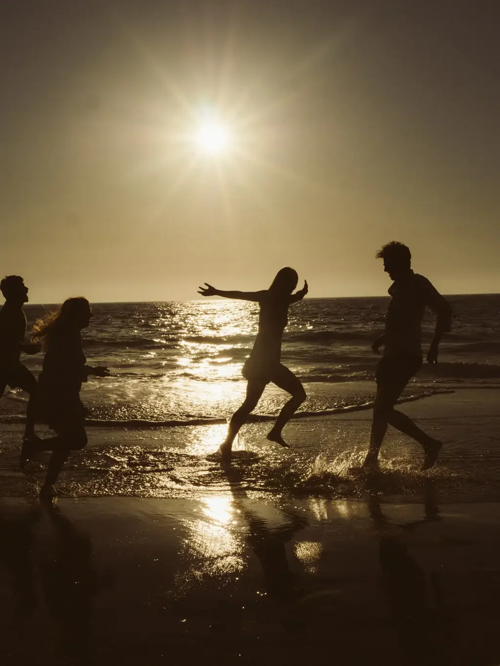 Silhouettes of four friends running and splashing through shoreline waves at sunset
