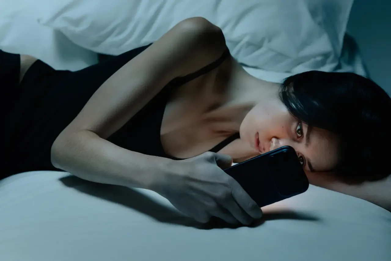 Woman in bed at night holding a glowing phone close to her face — the late-night self-research moment many women have before pursuing a late ADHD diagnosis.