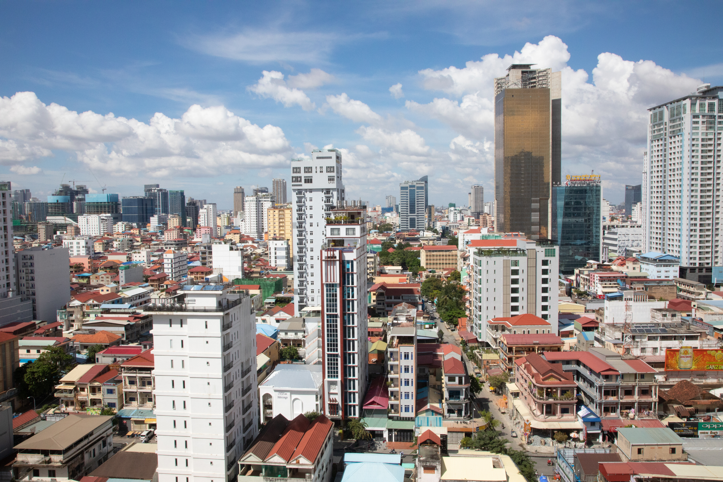 City skyline with tall buildings, skyscrapers, and residential houses under a partly cloudy blue sky.