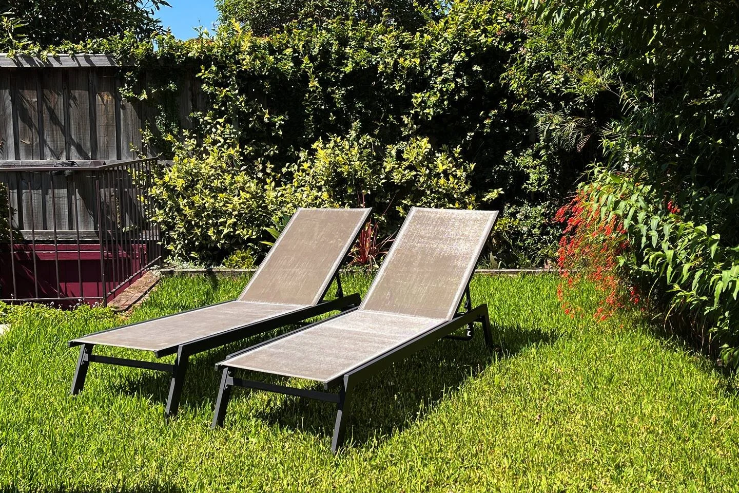 Two lounge chairs facing a lush garden with green grass, bushes, and trees under a sunny sky.