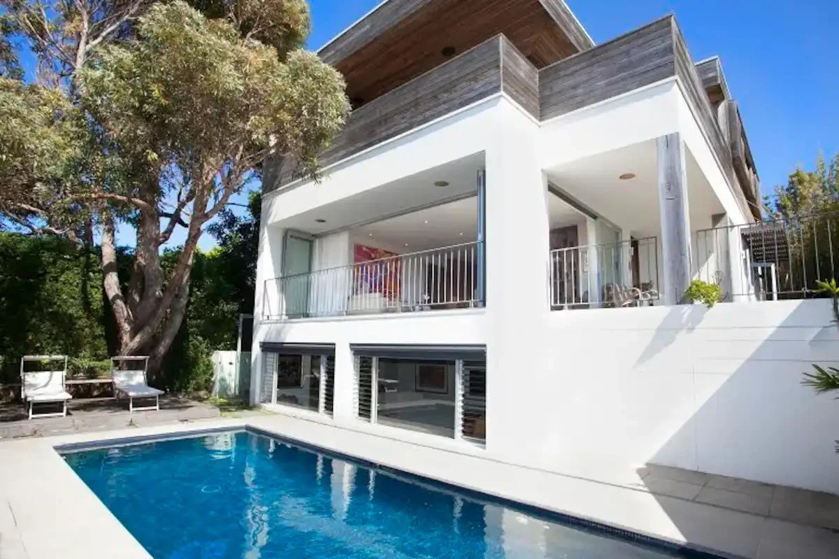 Modern white house with a swimming pool in the backyard, surrounded by trees and outdoor furniture.