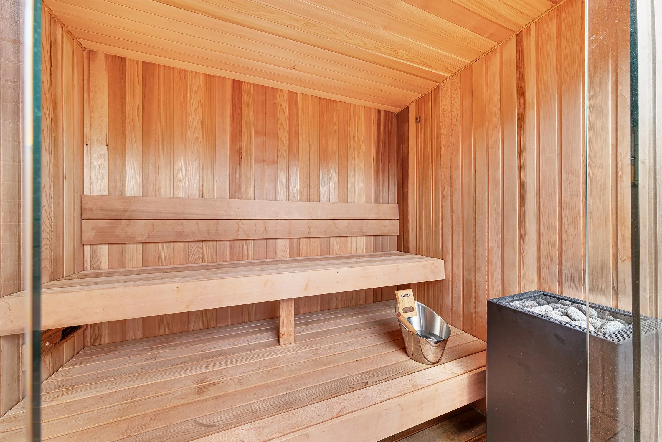 Interior of a traditional wooden sauna with wooden benches, a sauna heater with stones, and a wooden bucket with a ladle.
