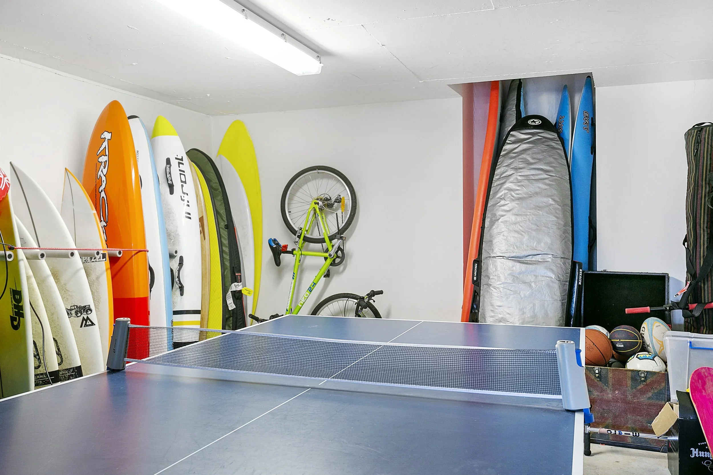 Garage with surfboards, bicycles, and sports equipment, and a ping pong table.