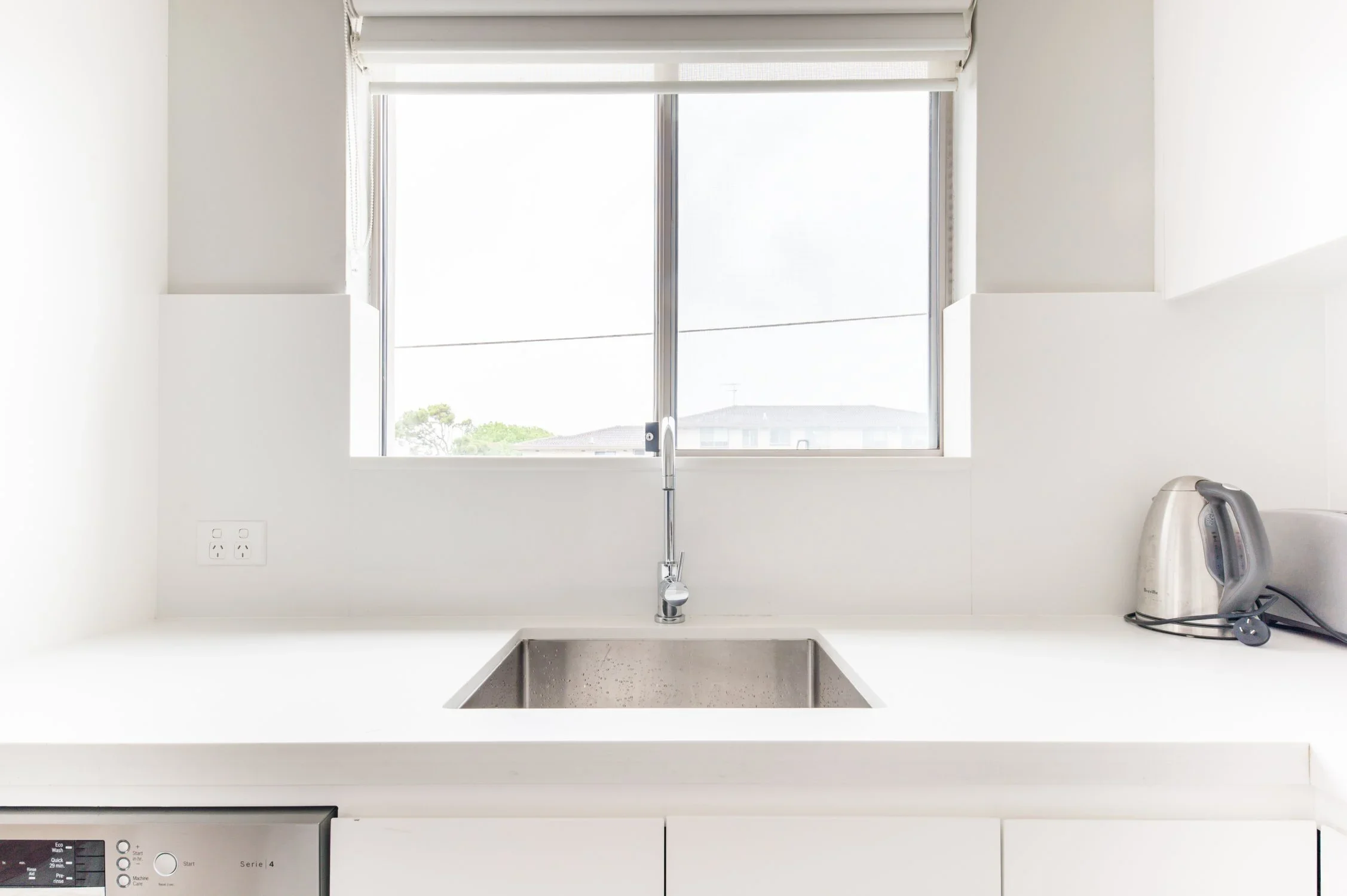 A kitchen countertop with a stainless steel sink in front of a window, with a toaster and an electric kettle on the right side.